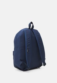 Mochila de tela azul marino con correas ajustables acolchadas, asa en la parte superior y bolsillo lateral. Superficie texturada con una forma elegante y redondeada.