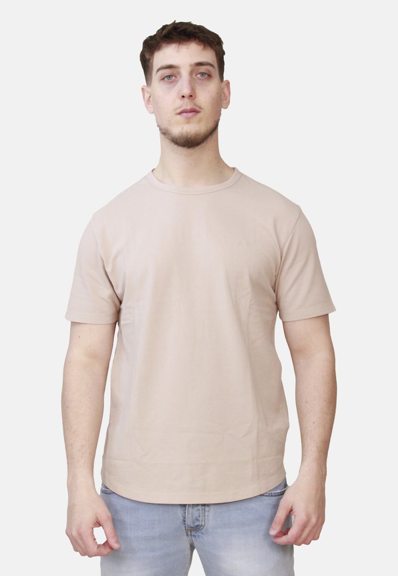 T-shirt beige chiaro, maniche corte, colletto rotondo, tessuto semplice, vestibilità casual. Indossato con jeans blu chiaro, senza loghi o motivi visibili.