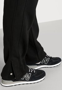 Czarne spodnie dresowe ze ściągaczami na suwak w połączeniu z czarnymi sneakersami New Balance posiadającymi teksturowany cholewkę i białą podeszwę.