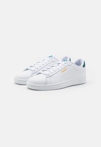 Sneakers atletici bianchi con materiale simile alla pelle, punta rotonda, suola piatta bianca, accenti turchesi sulla linguetta e sul tallone, dettaglio del logo dorato.