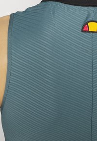 En strukturerad, teal sporttopp med tunna horisontella ränder, en svart krage och en cirkulär logotyp i rött och gult på baksidan.