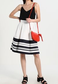 Un débardeur noir léger associé à une jupe blanche midi avec des rayures marines et un sac à main en cuir rouge. Sandales noires à volants.