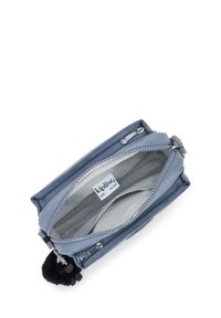 Borsetta blu chiaro con zip, caratterizzata da un esterno liscio, rivestimento in tessuto grigio e un accento di pompon nero. L'etichetta interna riporta la scritta "Kipling Live Light".