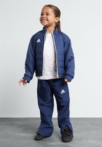 Marineblaue gepolsterte Jacke mit weißem Reißverschluss und Adidas-Logo, kombiniert mit passenden Hosen, verfügt über elastische Bündchen und einen lässigen Schnitt.