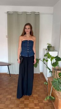 Top de denim sem mangas com uma silhueta ajustada e botões na frente, combinado com calças largas pretas. Clutch preta na mão.