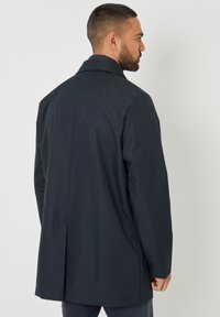 Mørk, vandtæt frakke med et rent design, mellem-længde snit og klassisk krave. Struktureret stof med minimal detaljering.