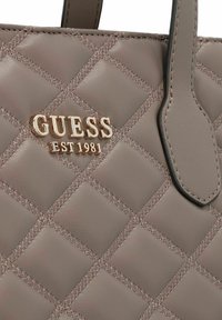 Gevoerde grijze faux leren handtas met gouden "GUESS EST 1981" logo. Kenmerkt een diamantpatroon en contrasterende stiksels. Inclusief bovenhandvatten.