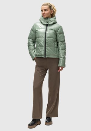 Groene pufferjack met een hoge kraag, ritsluiting en gestikte vierkanten. Gecombineerd met bruine wide-leg broeken en zwarte plateau laarzen.