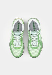Green and white athletic shoes with a mesh upper, perforated texture, reflective accents, and a cushioned sole. Laces are contrasting white.