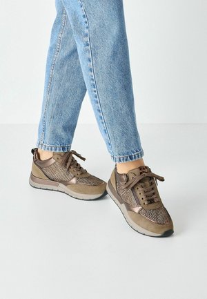 Bruine sneakers van mesh en suede, met een ronde neus, veters en contrasterende accenten. Gecombineerd met lichtblauwe opgerolde jeans.
