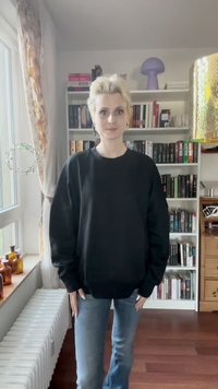 Černá oversized mikina s dlouhými rukávy a crew neckem, kombinovaná se světle modrými zvonovými džíny, na pozadí knihovny.