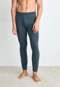 Šedé, přiléhavé dlouhé kalhoty vyrobené z měkké tkaniny s hladkým povrchem, které mají boční bílý pruh a design předního vaku.