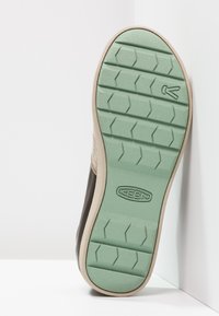 Hnědé boty s texturovaným koženým svrškem a světlou zelenou gumovou podrážkou s cik-cak vzorem a embosovaným logem.