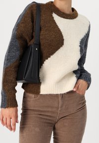 Stickad tröja med en färgblockdesign i bruna, krämfärgade och grå sektioner. Ribbad halsringning och ärmslut. Kombinerad med kordbyxor.