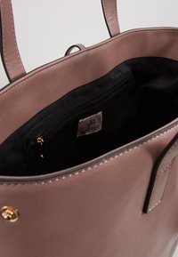 Sac à main mauve clair en similicuir lisse, doublure en tissu noir, poche intérieure zippée et détails en métal doré.
