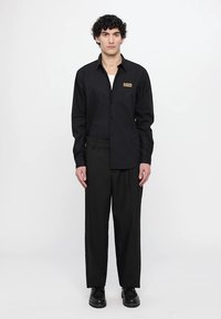 Black button-up shirt with long sleeves, front pocket, paired with black wide-leg trousers and black shoes. Simple, tailored design.