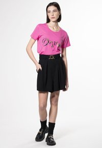 Camiseta de algodón rosa con el texto "Sueña", combinada con pantalones cortos negros de cintura alta con cintura fruncida y detalle de cinturón en tono dorado. Mocasines negros de suela gruesa.