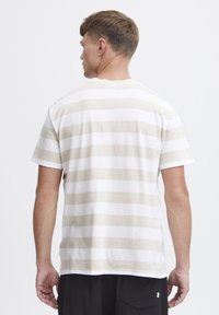 Camiseta de rayas con franjas horizontales beige y blancas, hecha de algodón, con mangas cortas y cuello redondo. Se muestra la vista trasera.