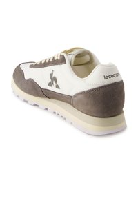 White sneaker with grey suede accents, textured surface, rounded toe, thin white laces, logo on side, and thick rubber sole.