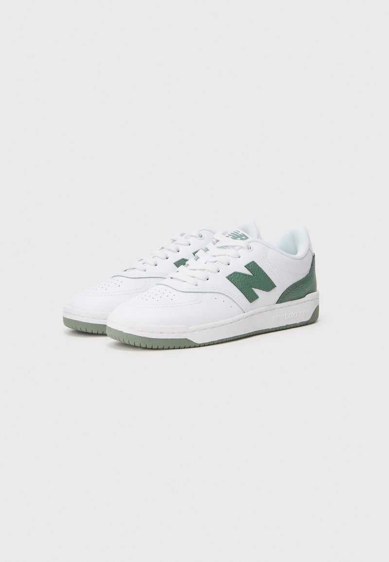 Zapatillas blancas con acentos verdes, que presentan una puntera perforada, paneles laterales texturizados y una suela de goma con un perfil bajo.