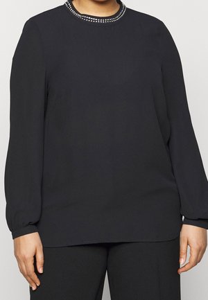 Blouse noire à manches longues avec un col rond agrémenté d'une rangée décorative de petites clous en argent le long du col. Texture de tissu lisse.