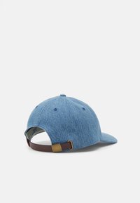 Boné de denim com aba curva, cor azul-claro, tecido texturizado e uma fita ajustável castanha com fivela metálica na parte de trás.