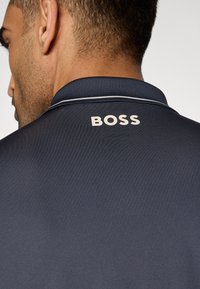 Μπλε πουκάμισο πόλο με υφή στο ύφασμα, με γιακά και λευκή λεπτομέρεια. Λογότυπο "BOSS" σε ανοιχτό μπεζ χρώμα στην πλάτη.