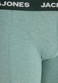 Gros plan sur un boxer homme vert clair avec une ceinture noire montrant partiellement le texte blanc du logo "JACK & JONES".
