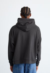 Mørkegrå hoodie med en afslappet pasform, der har en stor hætte, sænkede skuldre og ribbede manchetter. Kombineret med lyseblå denim shorts.