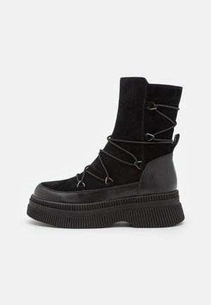 Botte plateforme noire mi-mollet avec tige en daim, talon en cuir, semelle épaisse à rainures et lacets croisés enroulés autour de la tige.