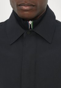 Sort jakke med en struktureret krave, udstyret med en farverig lynlås og en ribbet halsudskæring. Stoffet fremstår glat med minimal detaljer.