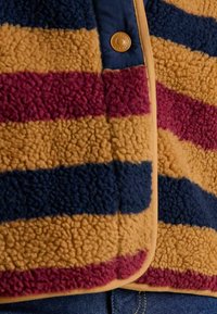 Koraļļu džemperis ar horizontālām svītrām sinepju dzeltenā, bordo un tumši zilā krāsā. Īpašības: teksturēta virsma un pogu aizdare.