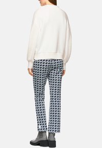 Cremefarbener Pullover mit strukturierten Schulterakzenten, kombiniert mit marineblauen, gemusterten Hosen. Das Ensemble wird durch graue Stiefeletten ergänzt.