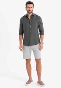 Chemise à manches longues gris foncé avec des boutons, associée à un short gris clair et des chaussures slip-on beige, présentant un design simple et épuré.