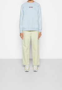 Sudadera azul claro con "WOOD" bordado en hilo oscuro. Combinada con pantalones sueltos de color verde pálido y zapatillas multicolores.