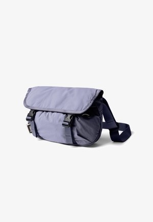 Petit sac bandoulière bleu marine avec rabat sécurisé par deux boucles noires à libération rapide et bandoulière réglable.