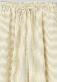 Pantalon beige ample avec de fines rayures verticales marron et un cordon de serrage noué à la taille élastique.