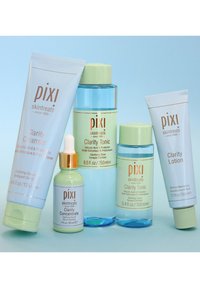 Fem hudpleieprodukter arrangert sammen: Clarity Cleanser (blå, rør), Clarity Tonic (grønn, flaske), Clarity Lotion (hvit, rør) og en serum.