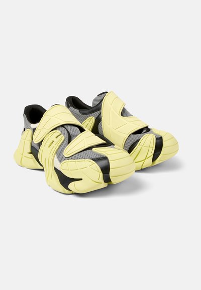 Black and yellow athletic shoes with a textured mesh upper, wide Velcro straps, and a thick rubber sole featuring unique patterns.