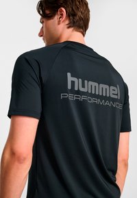 Svart funktionsjersey med texturerat mesh-tyg, korta ärmar och reflekterande "hummel PERFORMANCE"-text på baksidan.