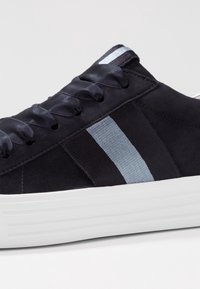 Mörk marinblå mockaskor med ljusblå rand, satin-snören och vit gummisula. Har en mjuk yta och en strömlinjeformad design.