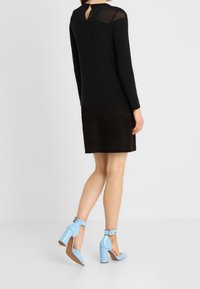 Černý dlouhý rukáv top s průsvitným zadním dílem, spojený s hnědou nubukovou sukní a světle modrými lakovými lodičkami na kotníkovém pásku se širokým podpatkem.