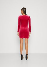Aansluitend lange mouwen jurk in levendig rood fluweel. Gladde textuur, knie-lengte, met een ronde halslijn en een bodycon silhoeet.