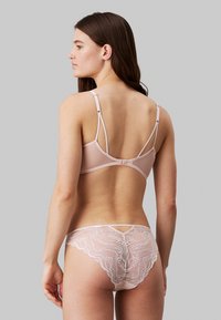 Ensemble de lingerie rose clair comprenant un soutien-gorge lisse avec des bretelles réglables et une culotte en dentelle avec des bords en vagues et des découpes.