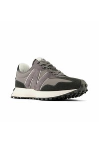 Chaussure de sport grise et noire avec logo "N" texturé sur le côté, semelle blanche et semelle extérieure noire à crampons, vue avant en angle.