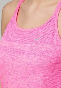 Gros plan d'une personne portant un haut de sport sans manches rose texturé avec un petit logo Nike réfléchissant sur la poitrine.