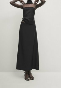 Black two-piece outfit featuring a strapless top with a side hoop detail and a full-length skirt. Smooth fabric with a flowing silhouette.