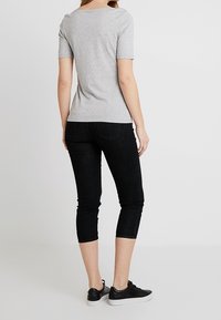 Grå kortærmet skjorte kombineret med sorte kapribukser. Outfitet har et enkelt design og en tætsiddende silhuet, suppleret med sorte sneakers.