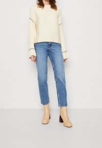 Cream ribbed sweater with wide sleeves, light blue straight-leg jeans, and beige block-heeled ankle boots with wooden accents.