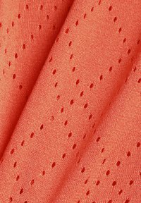 Tissu tricoté de couleur corail avec de petits trous perforés régulièrement espacés en motifs diagonaux, créant une surface texturée et respirante.